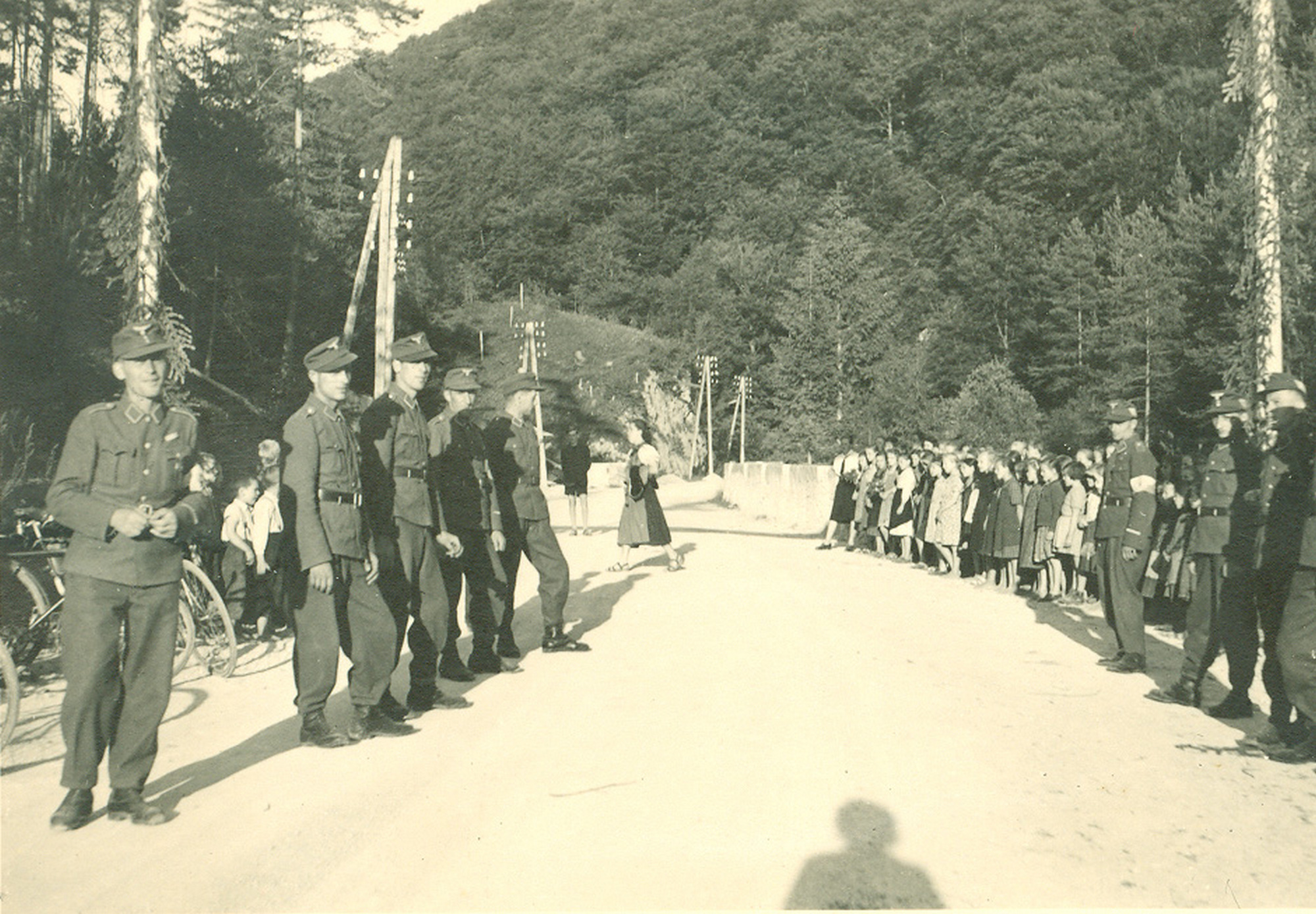 Slika 6: Vermani in učenci ob glavni cesti pričakujejo glavnega
                            finančnika in administratorja NSDAP Franza Xavierja Schwarza in
                            gavlajterja dr. Siegfrieda Uiberreitherja, 22. junij 1942 