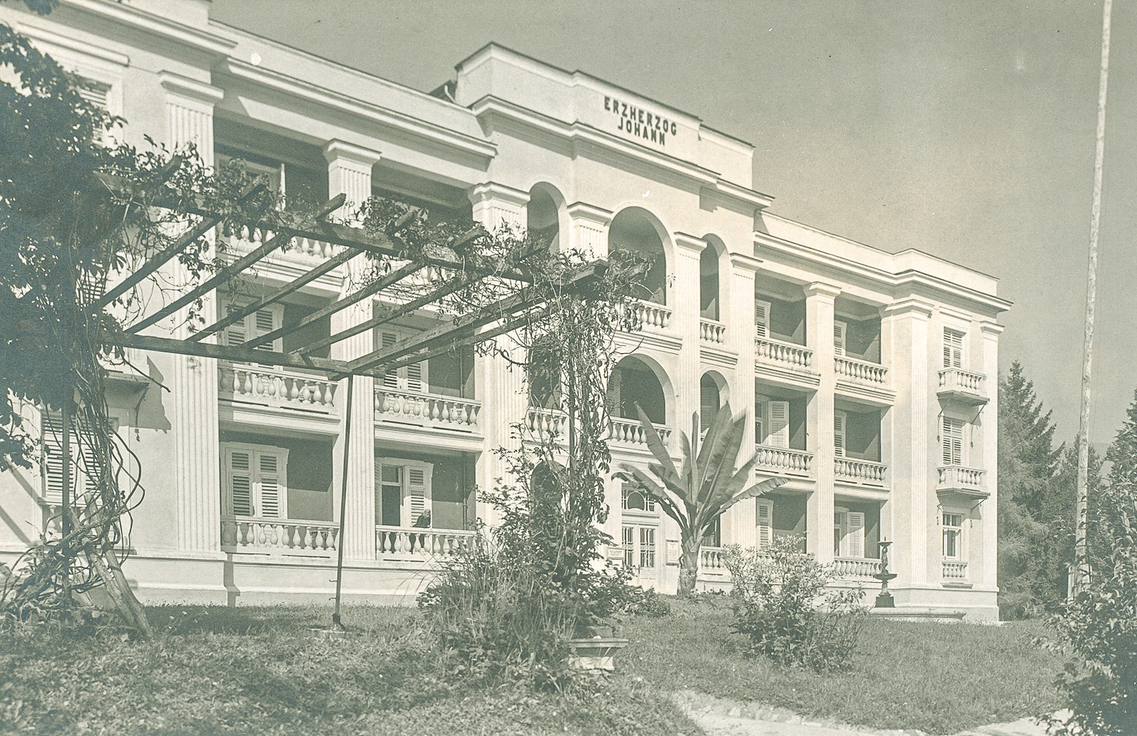 Slika 2: Hotel Erzherzog Johann kmalu po nemški zasedbi leta 1941. Desno od vhodnih vrat se pod povečavo vidi tudi pozdravna tabla z orlom, ki drži oljčni venec s svastiko. Na vzhodni strani stavbe je bil postavljen visok leseni steber, s katerega je plapolala nacistična zastava. Večji del stavbe je do danes ohranil nespremenjeno podobo, zgolj zahodno krilo se je razširilo in modificiralo z izgradnjo novega veznega objekta.